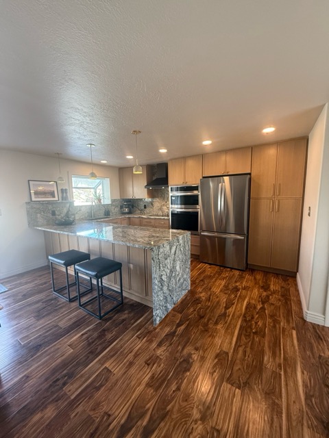 The same kitchen rebuilt with rift white-oak cabinets, a granite waterfall peninsula and dark acacia hardwood
