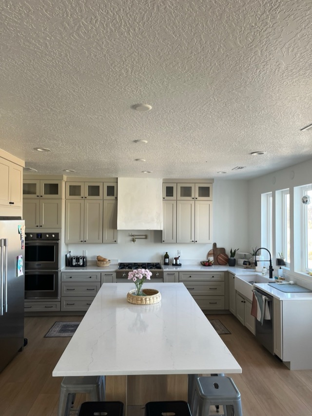 Cream kitchen with quartz island, custom range hood, and farmhouse sink