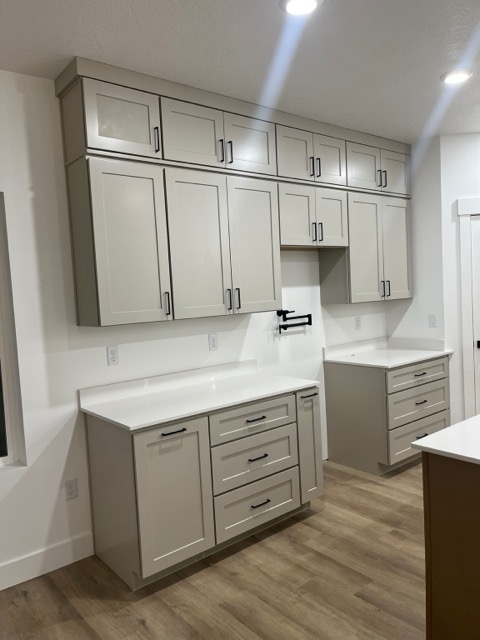 Stacked greige shaker wall cabinets over white quartz with a matte black wall-mounted pot filler