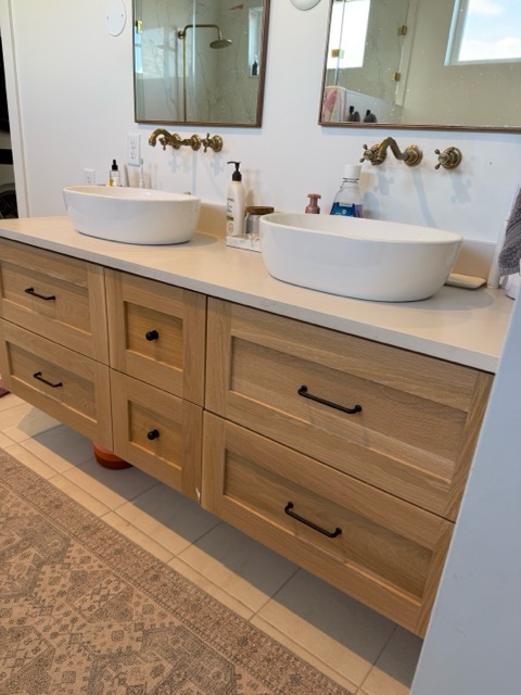 Floating white-oak shaker double vanity with a white quartz top, twin vessel sinks and aged brass wall-mount faucets