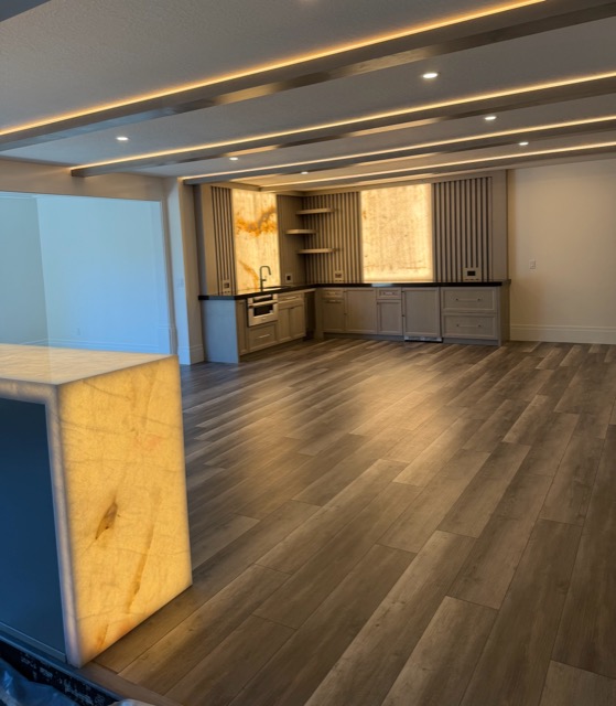Illuminated onyx waterfall end panel on a navy bar island, with the backlit wet bar beyond