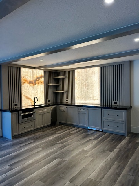 Corner of the wet bar with a full-height stained cabinet tower, floating shelves and backlit onyx accent panels