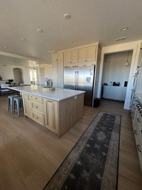 Natural white oak kitchen island with white quartz beside cream painted shaker cabinets and a built-in refrigerator