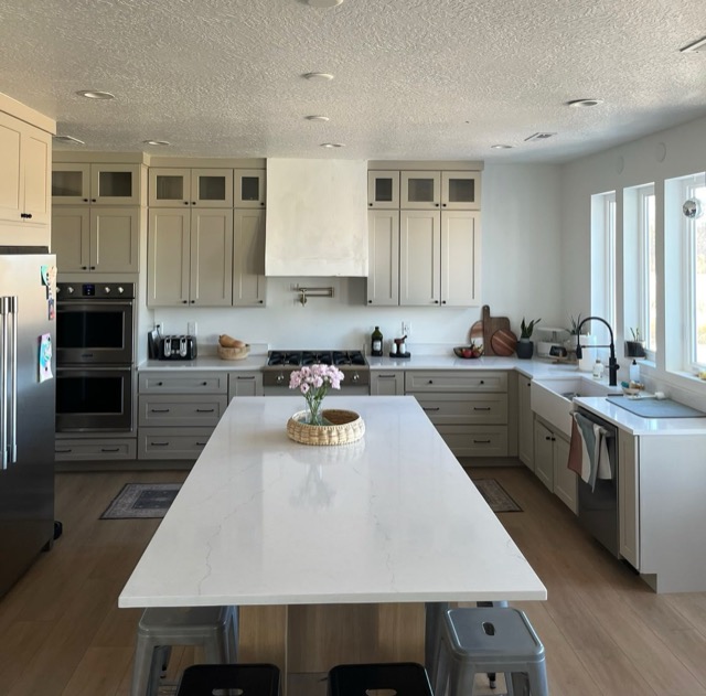 Greige shaker cabinets with glass mullion uppers, a white plaster hood and a brass pot filler over the cooktop
