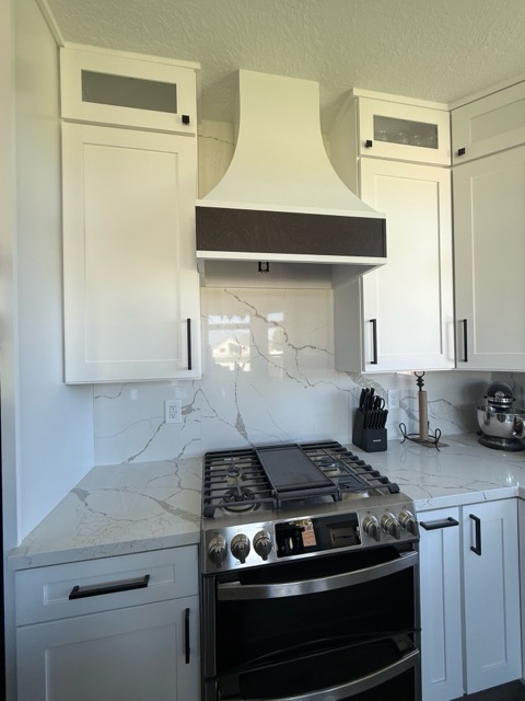Curved white plaster range hood with a dark walnut band over a gas range and full-height Calacatta quartz slab